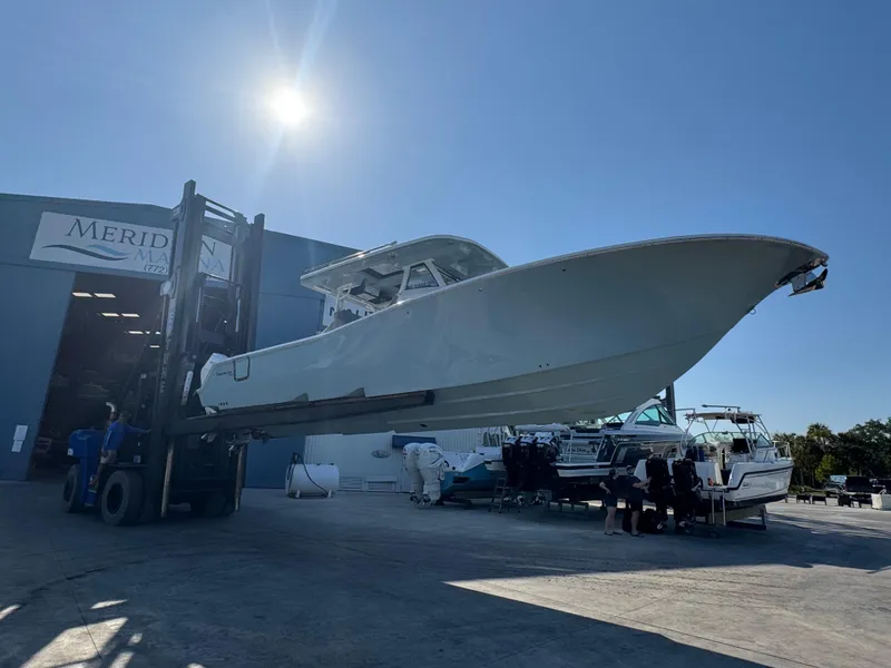 Slide: The Image of 2024 Tidewater 380 CC Adventure boat being lifted outside a marina under a clear blue sky. - 2