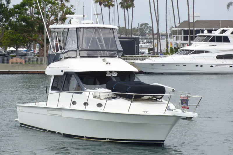 Slide: The Image of 2003 Mediterranean 38 Convertible yacht docked in marina, surrounded by palm trees and other boats. - 2