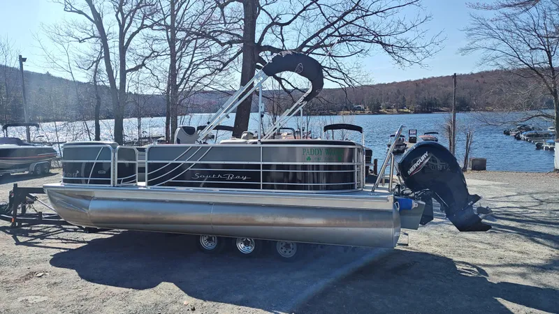 Slide: The Image of 2022 South Bay 200 Series S222RS pontoon boat by a lake, with Mercury outboard motor. - 3