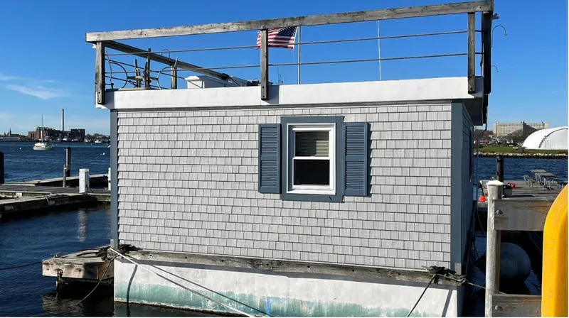 Slide: The Image of Custom 1990 houseboat with gray siding, docked by the waterfront, featuring a small window and rooftop railing. - 4