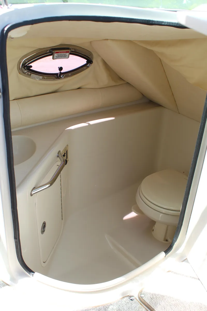 Slide: The Image of 2007 Sea Ray 240 Sundeck interior with compact marine toilet and porthole window. - 13