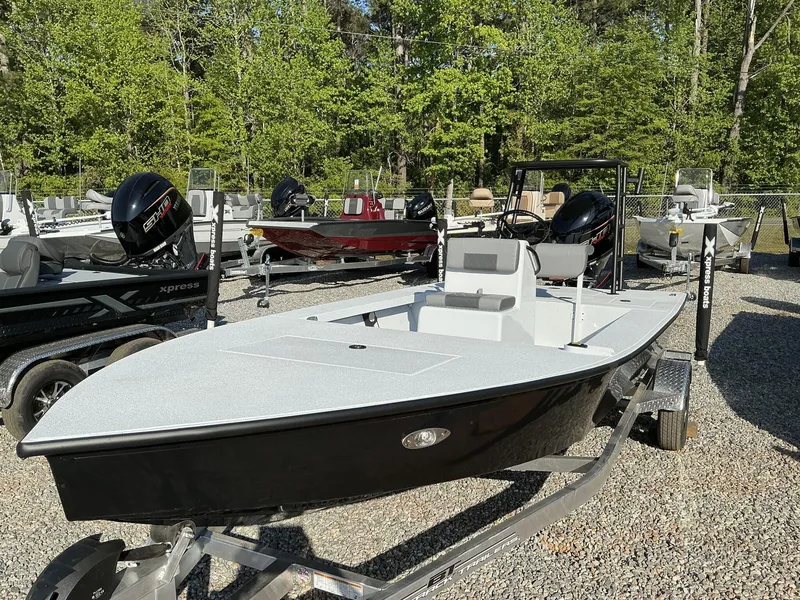 Slide: The Image of 2025 Xpress Skiff 185 boat on trailer, surrounded by trees and other boats. - 2