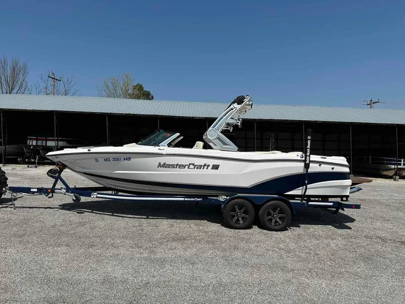 Slide: The Image of 2022 MasterCraft XT25 boat on trailer, parked outdoors under clear blue sky. - 1
