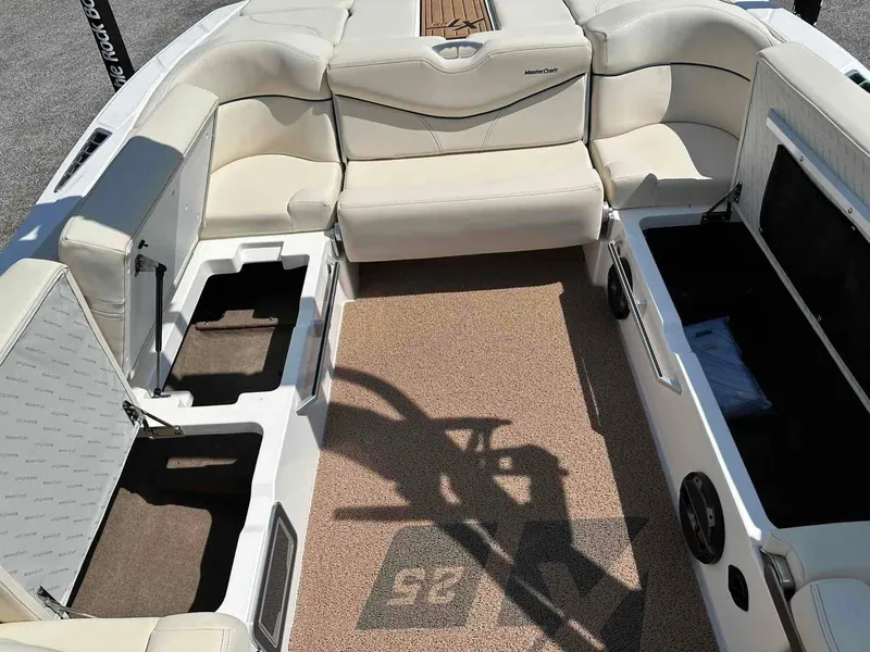 Slide: The Image of 2022 MasterCraft XT25 boat interior with open storage compartments and beige seating. - 12