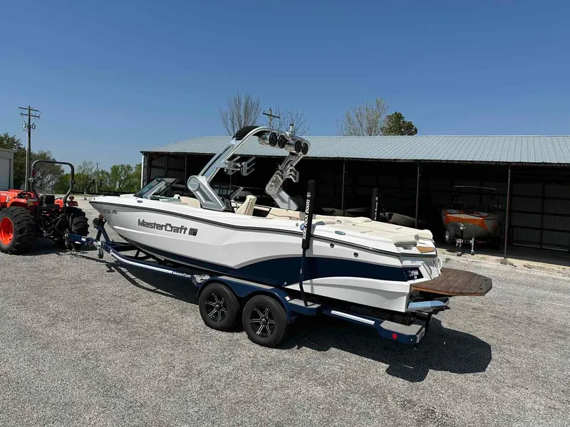 Slide: The Image of 2022 MasterCraft XT25 boat on trailer, parked outdoors near a shed. - 2