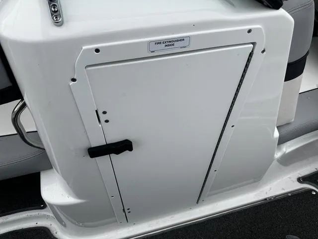 Slide: The Image of 2012 Yamaha Boats 212X fire extinguisher compartment, white panel with handle and label. - 16