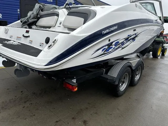 Slide: The Image of 2012 Yamaha Boats 212X on trailer, twin engine, white with blue graphics, parked outdoors. - 5