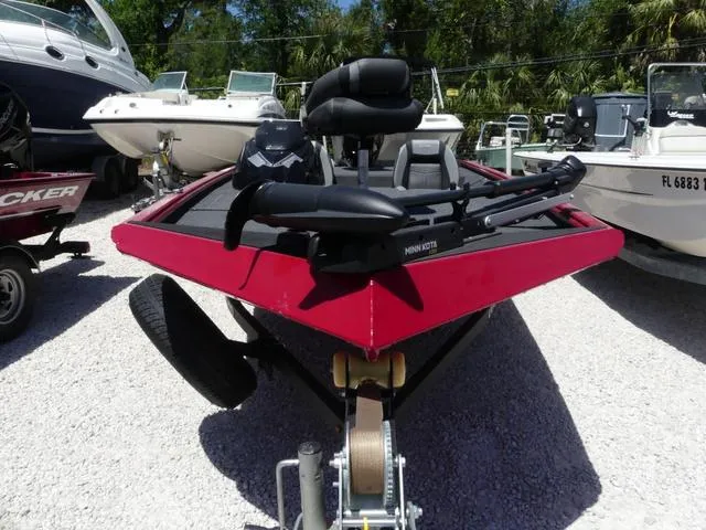 Slide: The Image of 2022 Lund 2175 Pro V boat in red, parked on gravel, with other boats nearby. - 2