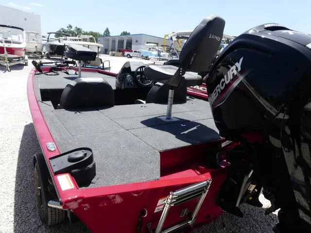 Slide: The Image of 2022 Lund 2175 Pro V boat with Mercury engine, red exterior, parked on gravel. - 4