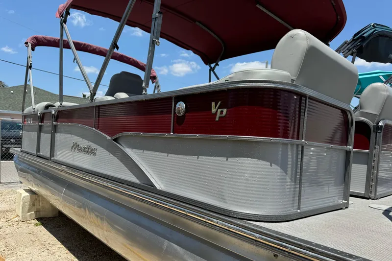Slide: The Image of 2022 Manitou Oasis SR VP pontoon boat with red and gray design, docked under a blue sky. - 19