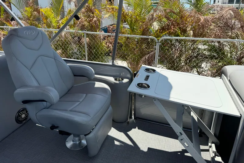 Slide: The Image of 2022 Manitou Oasis SR VP boat interior with gray captain's chair and foldable table. - 9