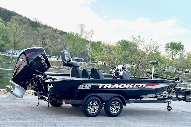 Slide: The Image of 2025 Tracker Savage 215 boat on trailer, parked near a scenic lake with trees. - 122