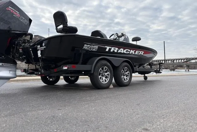 Slide: The Image of 2025 Tracker Savage 215 boat on trailer, parked near a bridge under cloudy skies. - 130