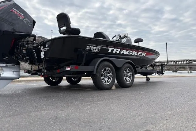Slide: The Image of 2025 Tracker Savage 215 boat on trailer, parked near a bridge under cloudy skies. - 133
