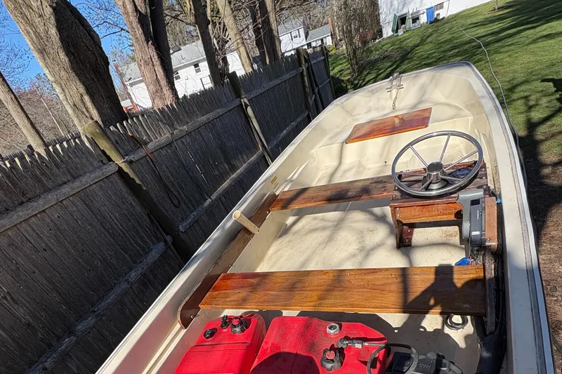 Slide: The Image of 1987 Boston Whaler 13 boat with wooden seats and steering wheel, parked outdoors. - 13