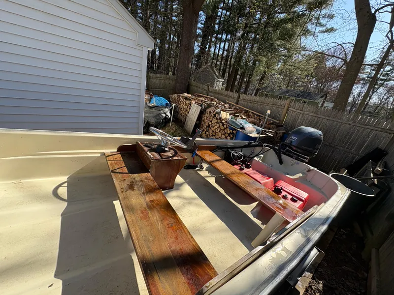 Slide: The Image of 1987 Boston Whaler 13 boat with wooden seats, outboard motor, and storage area in a backyard setting. - 4