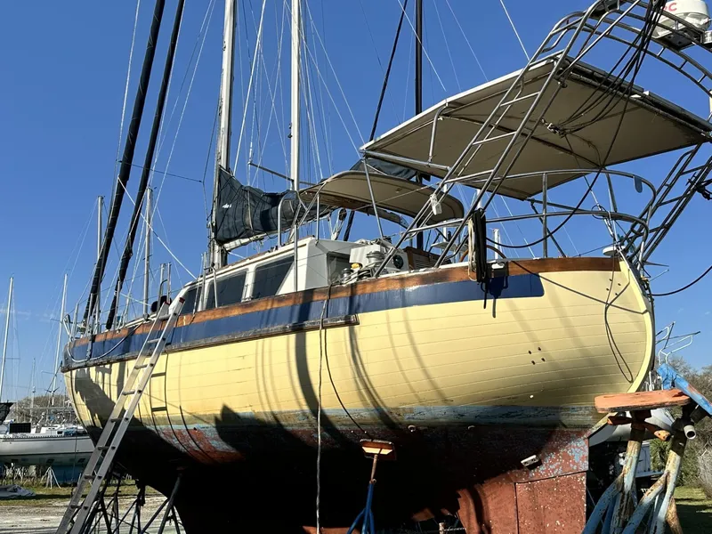 Slide: The Image of 1986 Slocum 43 sailboat on dry dock, yellow hull, blue stripe, clear sky background. - 1