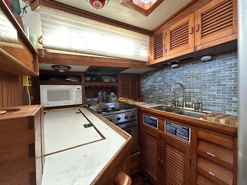 Slide: The Image of 1986 Slocum 43 yacht kitchen with wooden cabinets, microwave, stove, and tiled backsplash. - 13