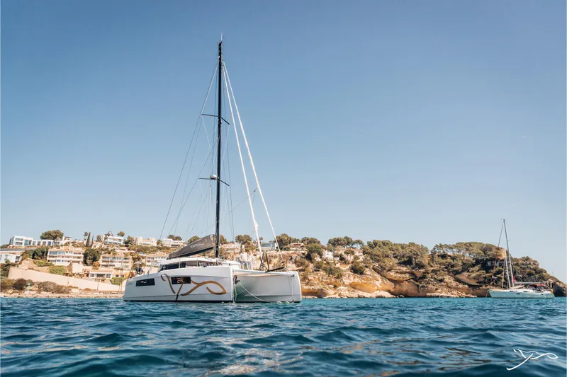 Slide: The Image of 2025 Nautitech 44 Open catamaran sailing near a scenic coastal landscape. - 1