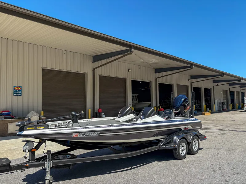 Slide: The Image of 2014 Skeeter FX 21 boat on trailer outside a large garage under clear blue sky. - 1