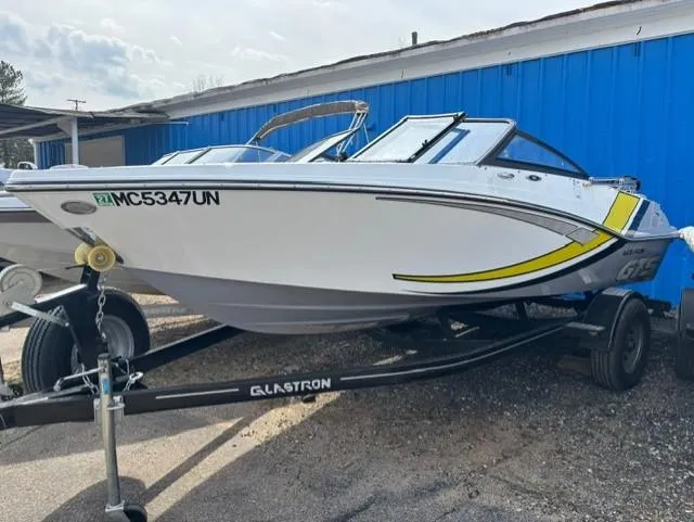 Slide: The Image of 2021 Glastron GTS 185 boat on trailer, white with yellow accents, parked outdoors. - 12