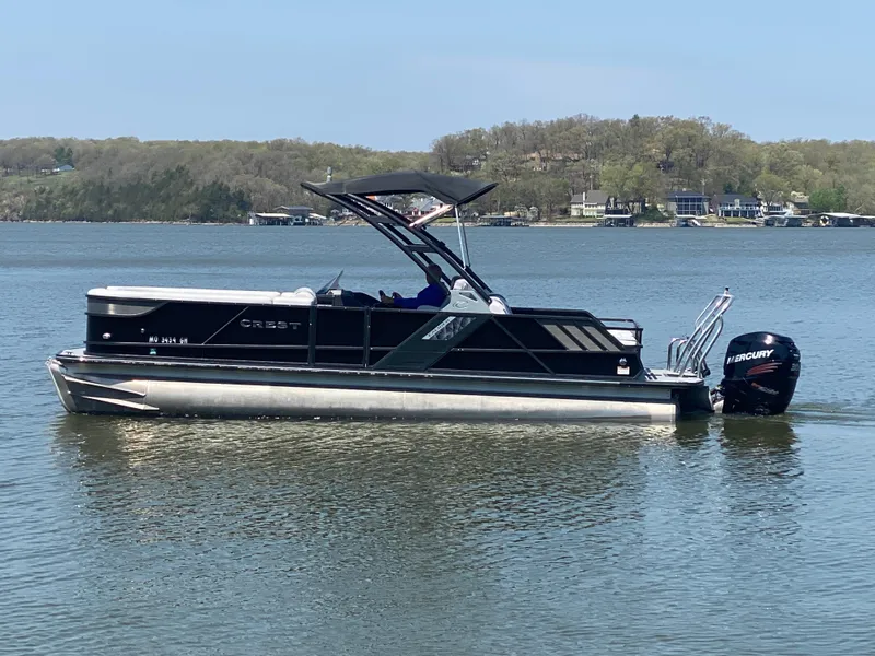 Slide: The Image of 2018 Crest Caliber 250 SLRC pontoon boat on a calm lake with scenic background. - 2
