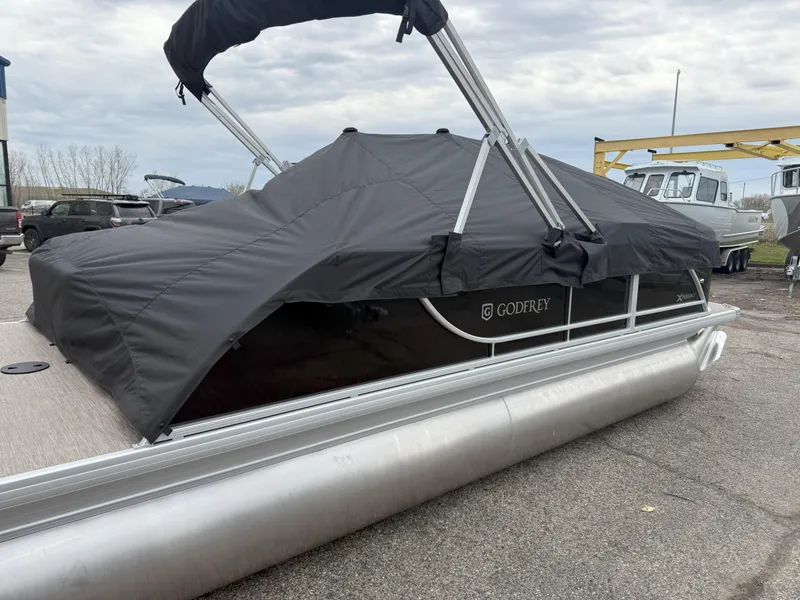 Slide: The Image of 2025 Godfrey EX2086SFLX pontoon boat with black cover, parked on a lot. - 5