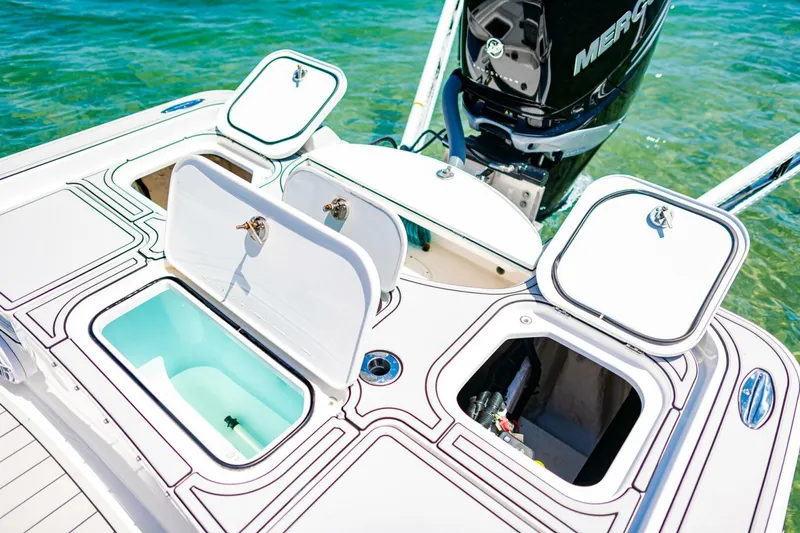 Slide: The Image of 2023 Contender 25 Bay boat with open storage compartments and outboard motor in clear water. - 25