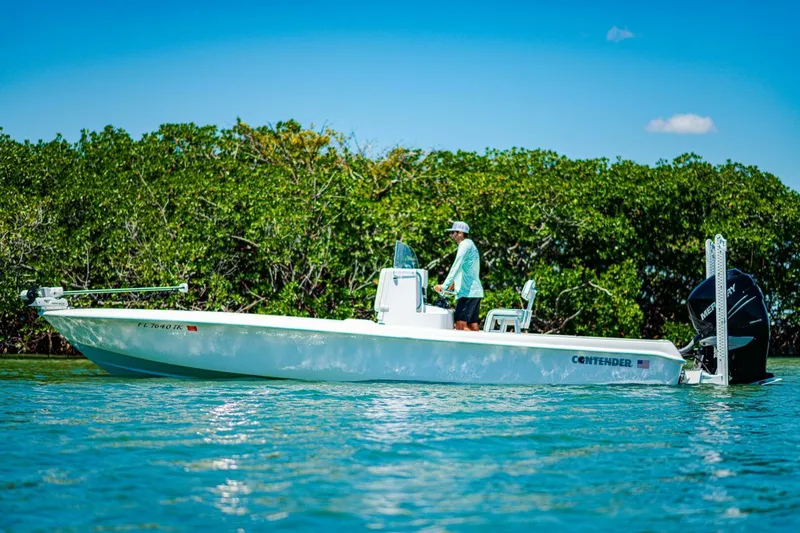 Slide: The Image of 2023 Contender 25 Bay boat on water, person standing, lush greenery background. - 36