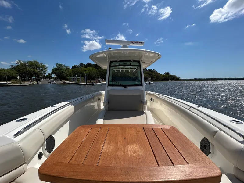 Slide: The Image of 2021 Boston Whaler 330 Outrage boat on water, featuring a wooden table and clear sky. - 17