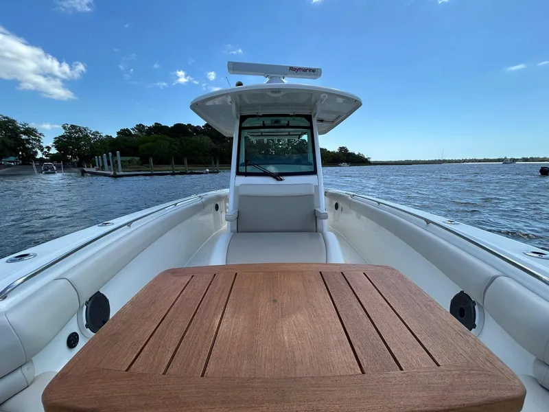 Slide: The Image of 2021 Boston Whaler 330 Outrage boat on water, featuring spacious deck and wooden table. - 18