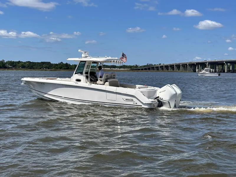 Slide: The Image of 2021 Boston Whaler 330 Outrage boat cruising on a sunny day near a bridge. - 2