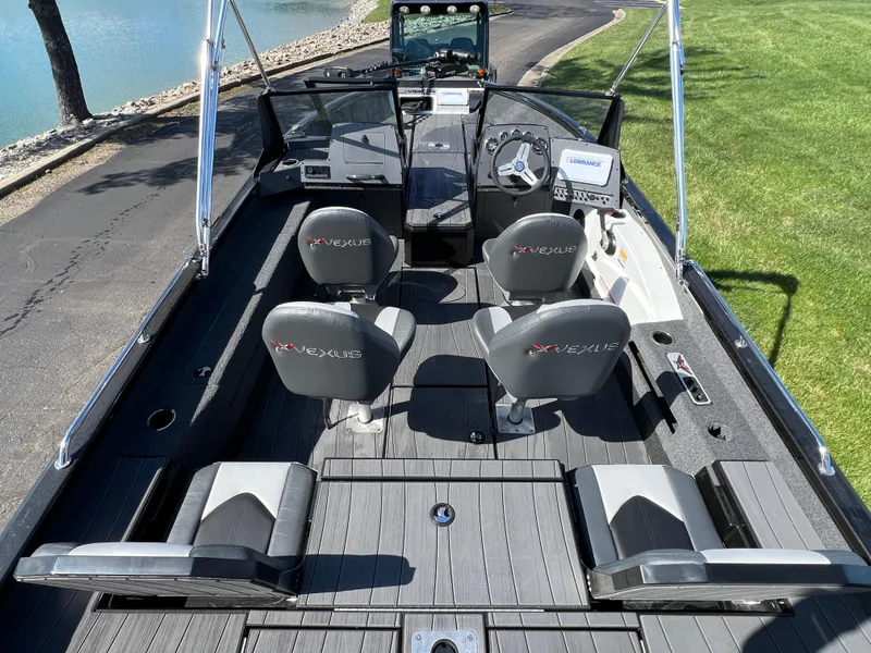 Slide: The Image of 2025 Vexus ADX190 boat interior with seating and steering, parked by a lake. - 12