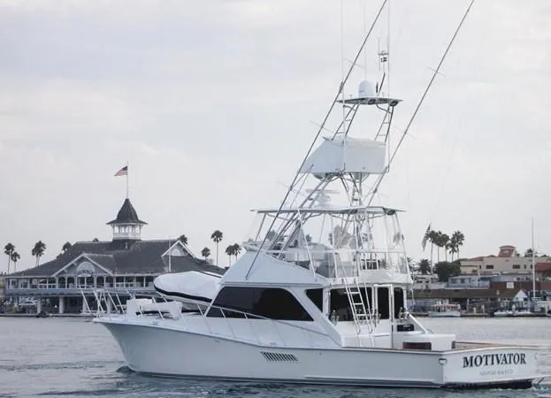 The Image of 1982 Pacifica Convertible yacht "Motivator" near a marina with palm trees and a historic building. - 1
