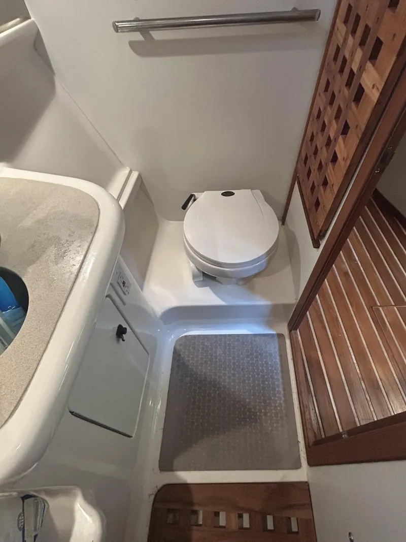 Slide: The Image of 1998 Pursuit 3400 Express boat bathroom with toilet, sink, and wooden flooring. - 12