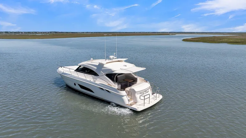 Slide: The Image of 2020 Riviera 4800 Sport Yacht cruising on a serene waterway under a clear blue sky. - 11