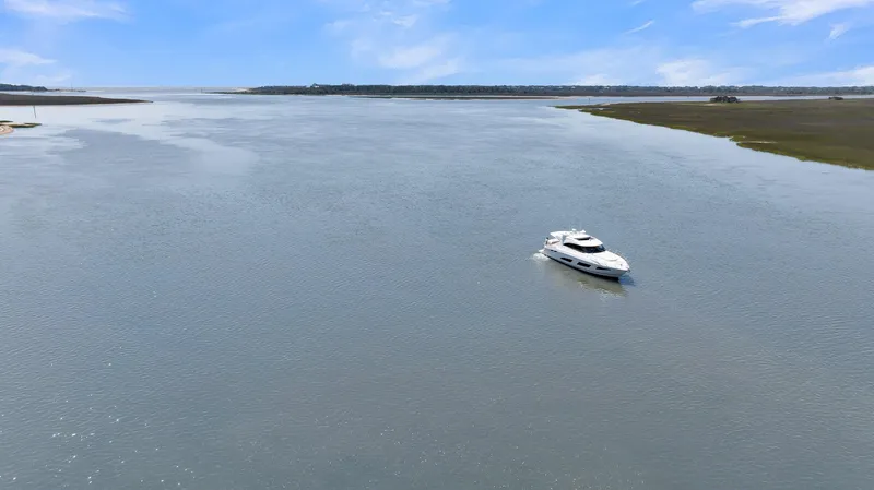 Slide: The Image of A 2020 Riviera 4800 Sport Yacht cruising on a wide, tranquil river under a clear blue sky. - 13