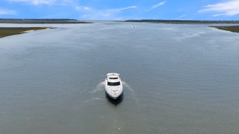 Slide: The Image of 2020 Riviera 4800 Sport Yacht cruising on a wide, calm river under a clear blue sky. - 15