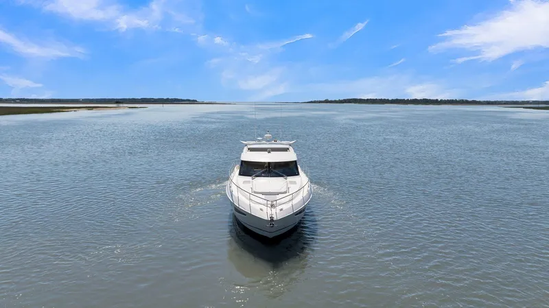 Slide: The Image of 2020 Riviera 4800 Sport Yacht cruising on a serene waterway under a clear blue sky. - 5