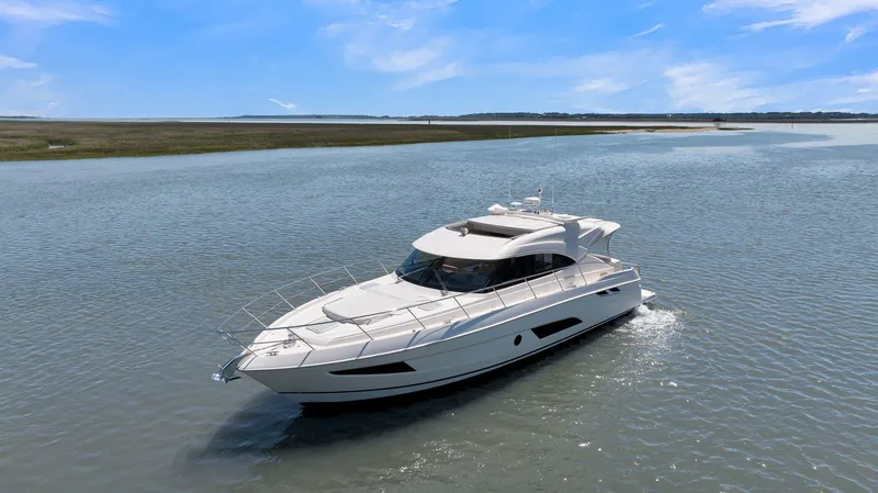 Slide: The Image of 2020 Riviera 4800 Sport Yacht cruising on a calm waterway under a clear blue sky. - 7