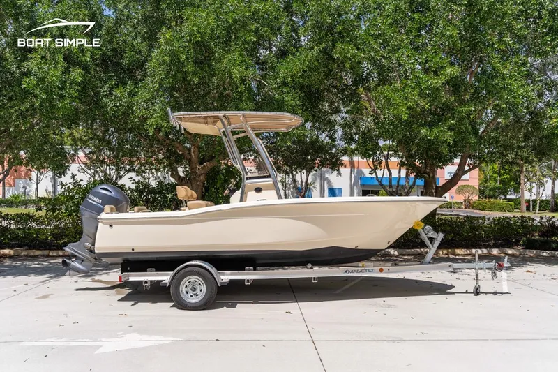 Slide: The Image of 2022 Scout 195 Sportfish boat on trailer, parked outdoors with trees in background. - 0