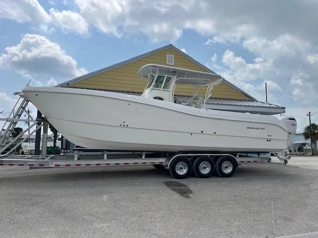 Slide: The Image of 2025 World Cat 325 CC boat on a trailer, parked near a yellow building under a cloudy sky. - 1