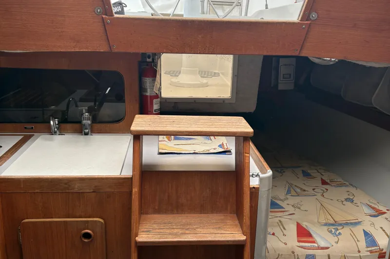 Slide: The Image of 1989 O'Day 272 sailboat interior with wooden steps, kitchenette, and nautical-themed bedding. - 14