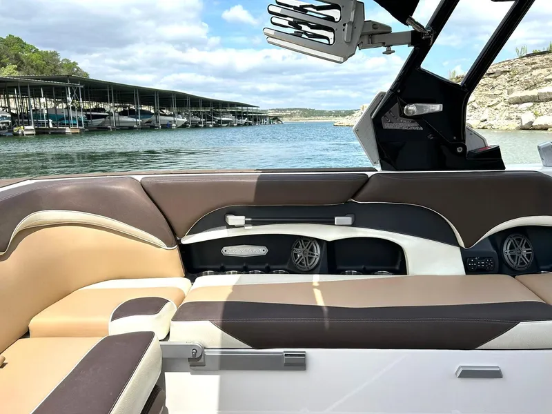 Slide: The Image of 2017 Supra SE 550 boat interior with brown and beige seating, docked by a scenic lake. - 31