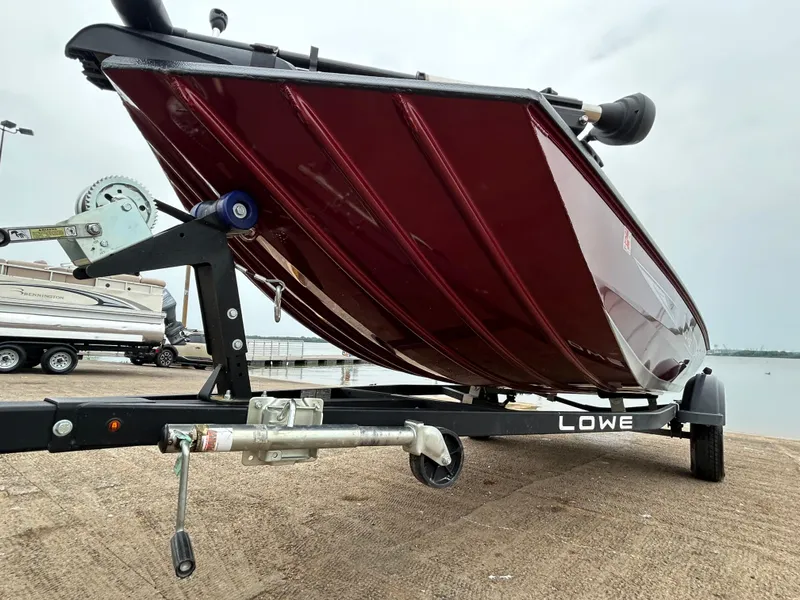 Slide: The Image of 2022 Lowe Skorpion 17 boat on trailer, red hull, parked near water. - 19