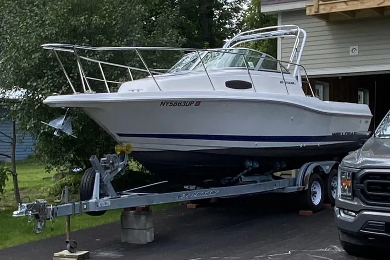 The Image of 1996 Wellcraft 23 Excel boat on trailer, parked in driveway near a house. - 1