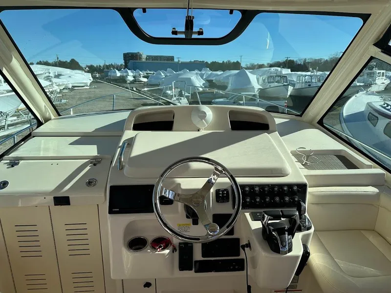 Slide: The Image of 2022 Grady-White Express 330 helm with steering wheel and controls, docked with boats in background. - 17