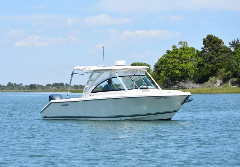 Slide: The Image of 2012 Pursuit DC 265 Dual Console boat on calm water near lush greenery. - 5