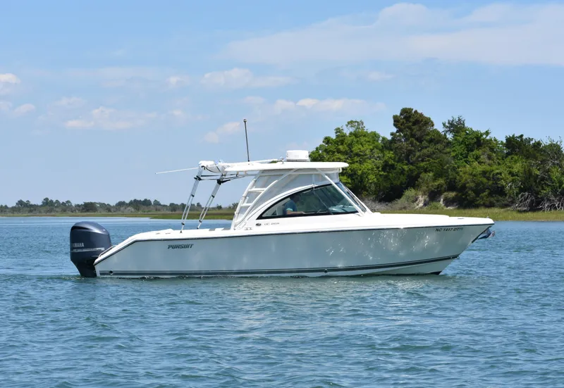 Slide: The Image of 2012 Pursuit DC 265 Dual Console boat on calm water near a green shoreline. - 6