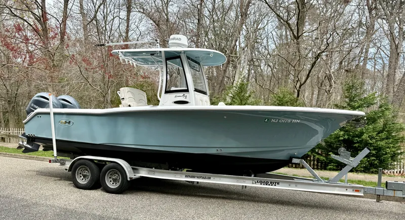 Slide: The Image of 2019 Sea Hunt Gamefish 25 boat on trailer, parked on a road with trees in background. - 33